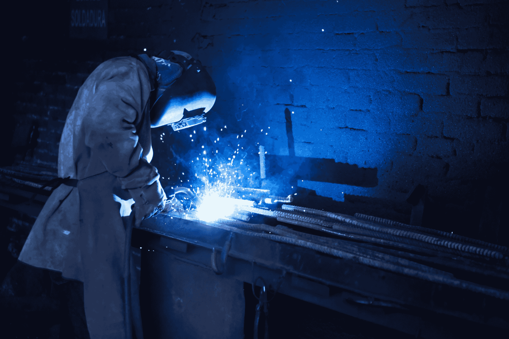 A person in protective welding gear (helmet, jacket) engaged in the skilled trade welding.