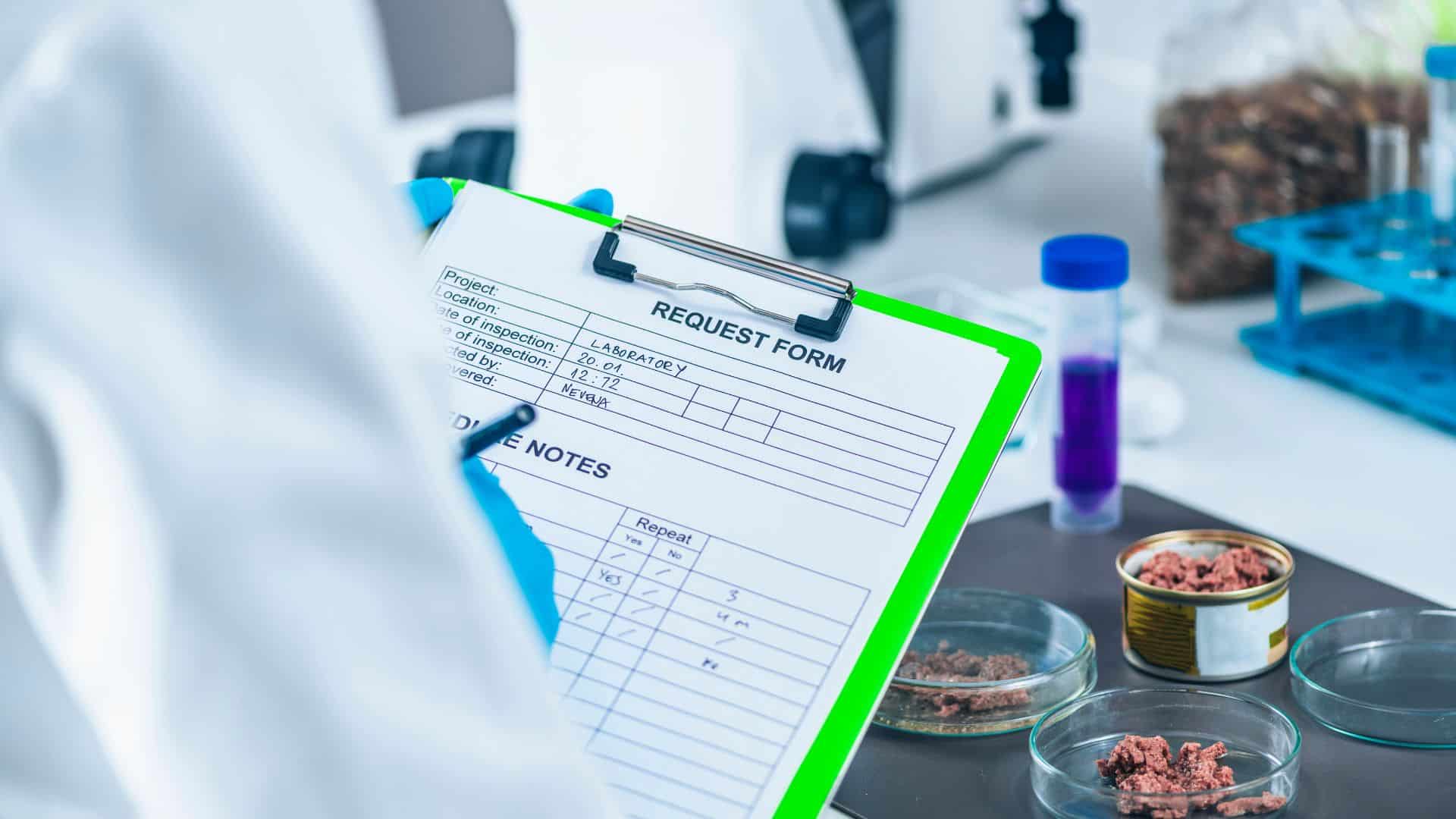 Close-up of a quality control technician in a lab analyzing canned food samples and recording results on a request form clipboard during a food safety inspection.