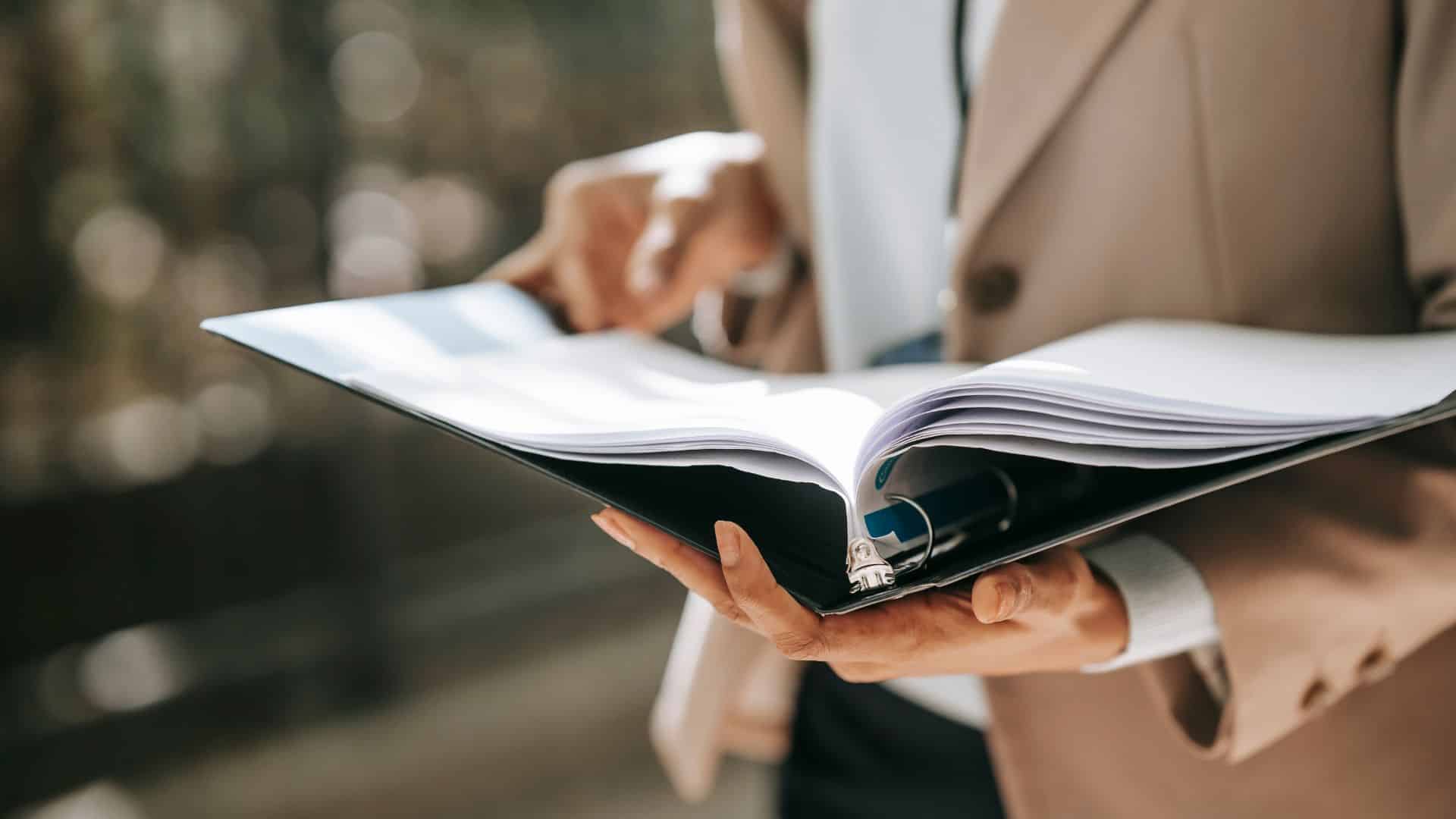 Close-up of a food regulatory specialist reviewing documents in a binder, ensuring compliance with food safety and labeling regulations.