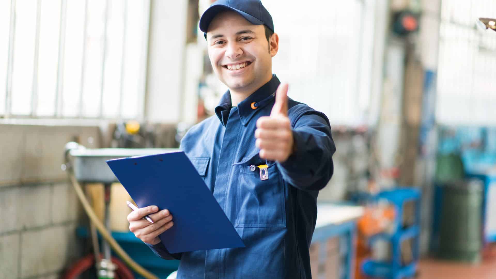 Millwright mechanic in a food processing facility smiling and giving a thumbs up while holding a clipboard, representing machinery maintenance and operational safety.