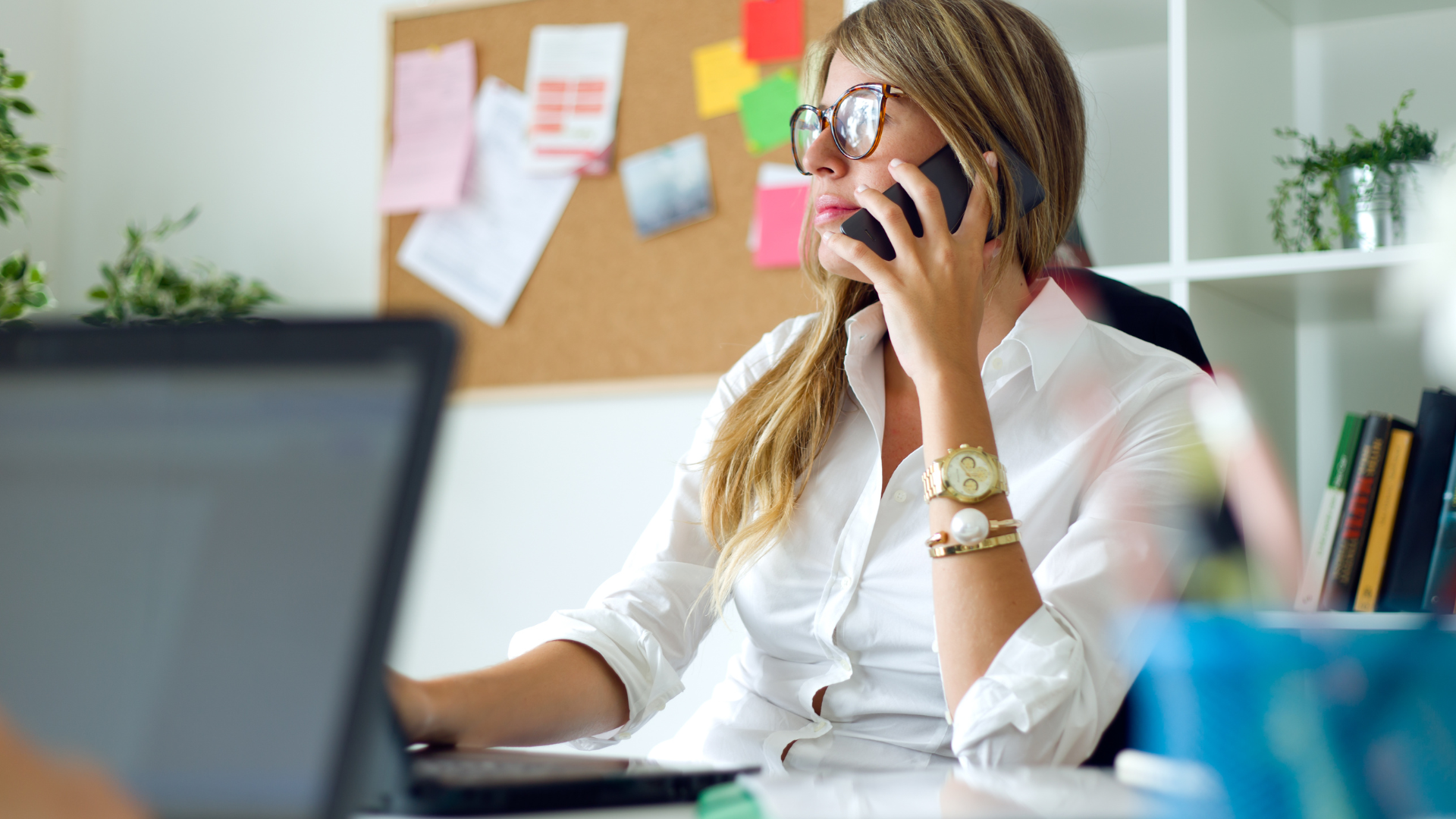 Food commodity procurement specialist on a phone call at her desk, managing supplier communication while working on a laptop in a modern office setting.