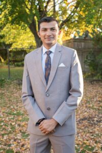 Rahul Mor in a suit standing from of orange fall leaves in a backyard