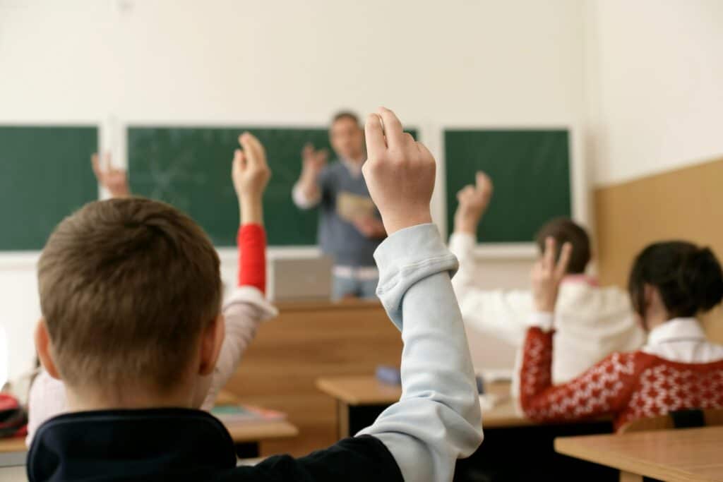 Photo of a Students Sitting in a Classroom with Raised Hands to Ask Questions